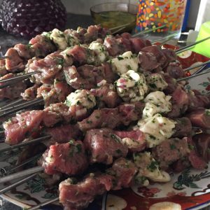 Several skewers of marinated and threaded cubes of meat and fat on a plate, waiting to be char grilled.
