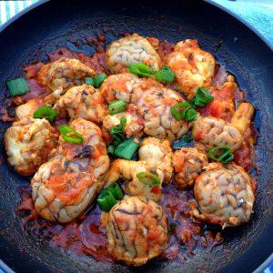 Overhead photo showing many pieces of beef brain in a pan. The offal was cooked in a reduced tomato sauce.