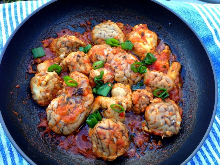 Overhead photo showing many pieces of beef brain in a pan. The offal was cooked in a reduced tomato sauce.