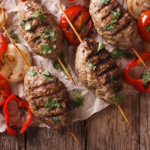 overhead image of kefta brochettes on wood table with grilled onions and tomatoes