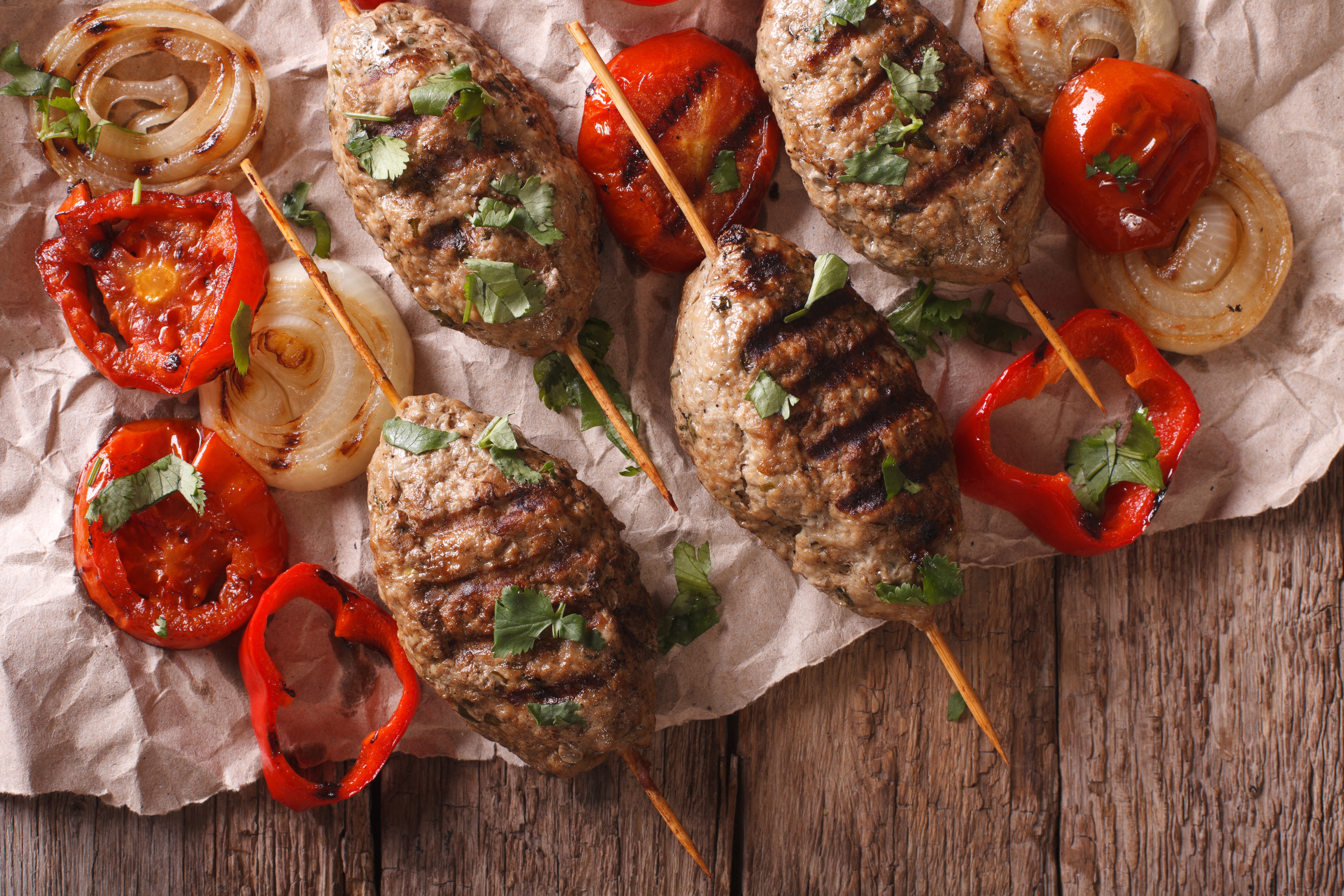 overhead image of kefta brochettes on wood table with grilled onions and tomatoes