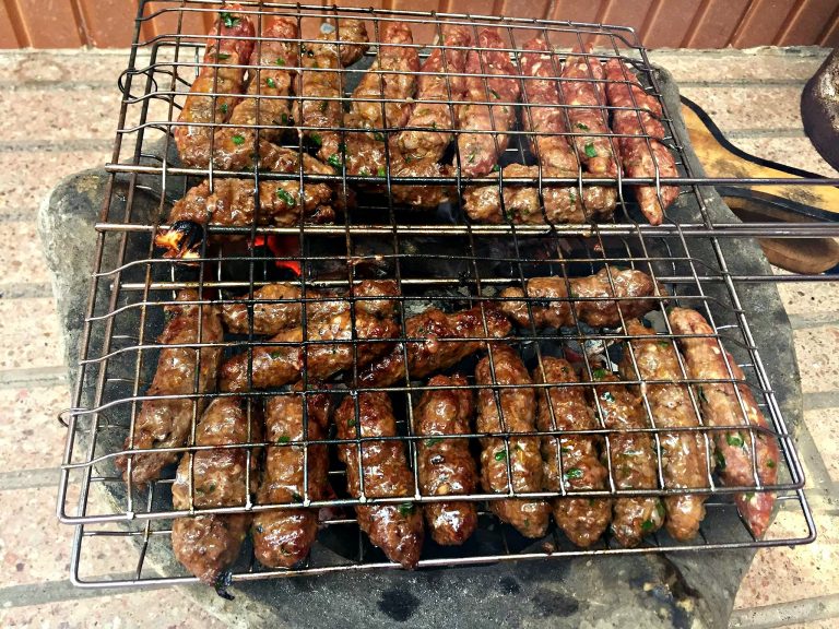 Photograph of grill basket full of kefta as the meat cooks over hot charcoal.