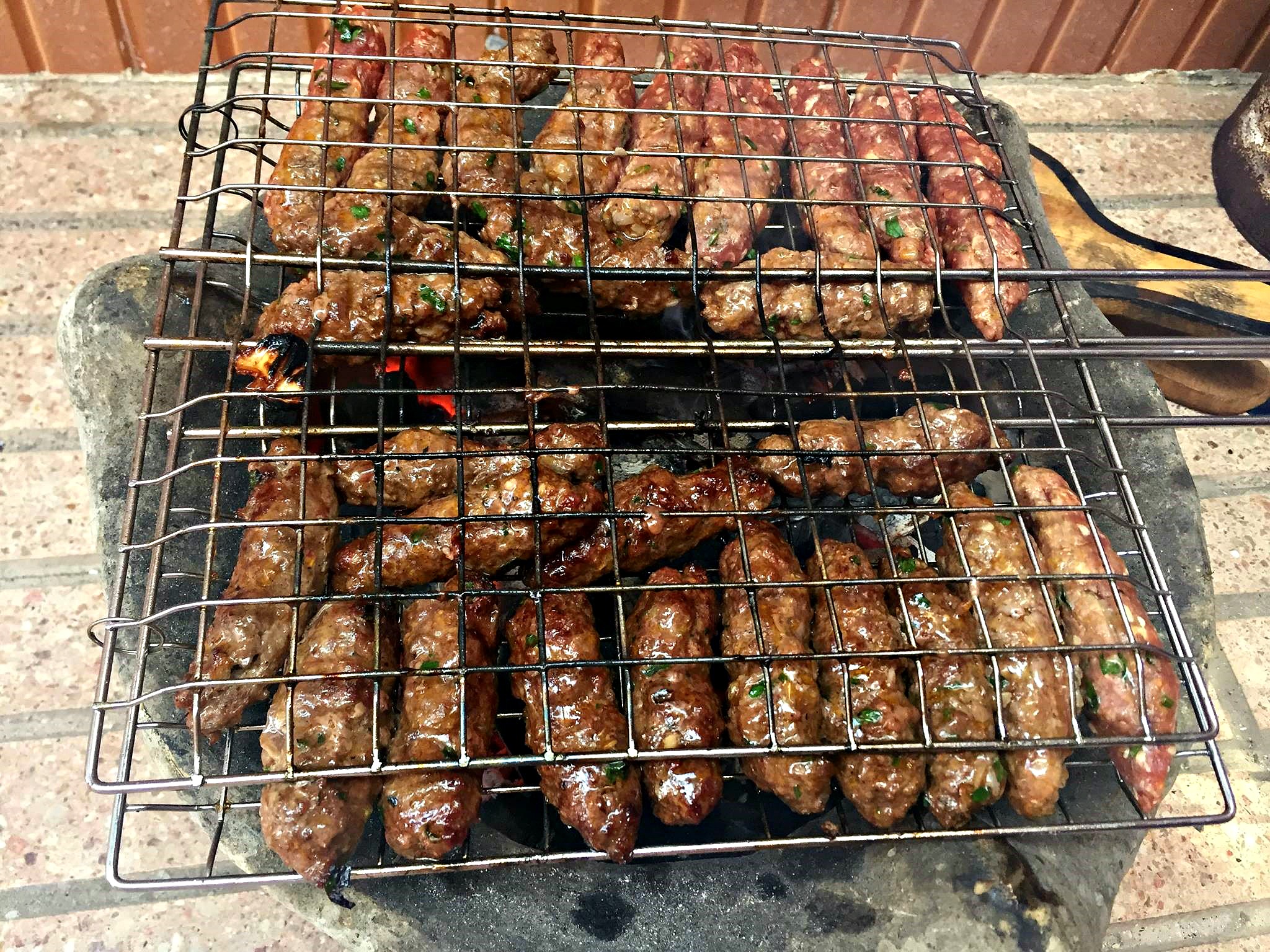 Photograph of grill basket full of kefta as the meat cooks over hot charcoal.