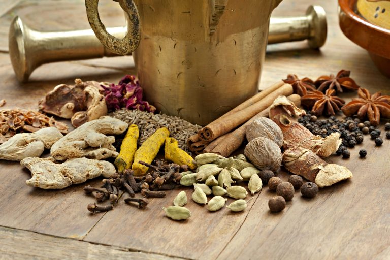 Image showing dry spices used to make ras el hanout at the base of a brass mortar and pestle.