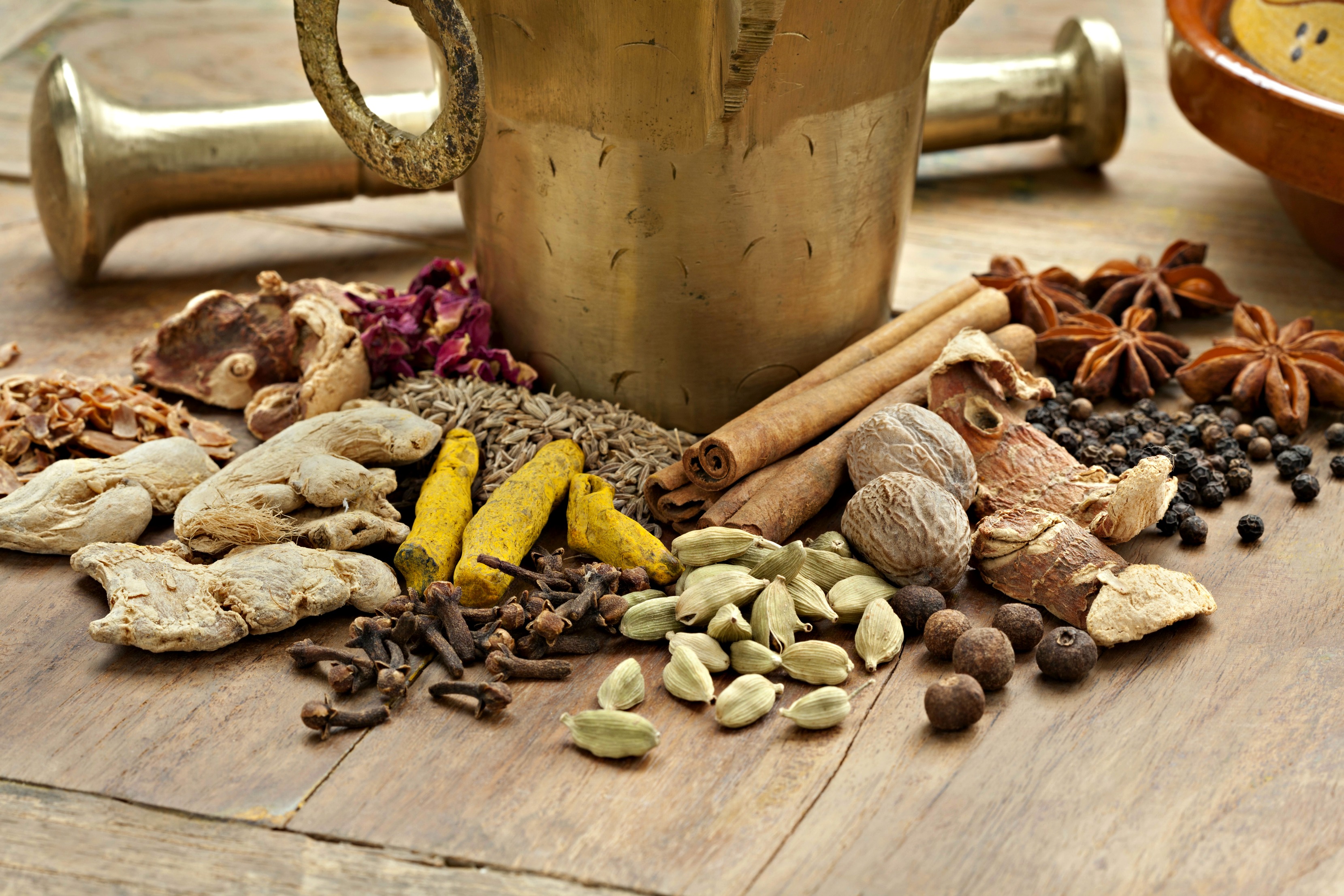 Image showing dry spices used to make ras el hanout at the base of a brass mortar and pestle.
