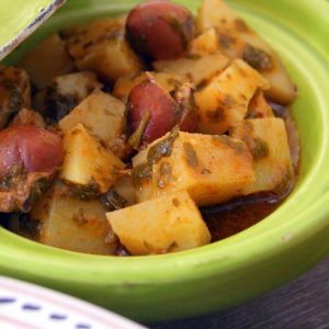 Moroccan potato salad with chermoula. The potatoes are cut in cubes and coated with chermoula, served in a green plate and decorated with purple olives