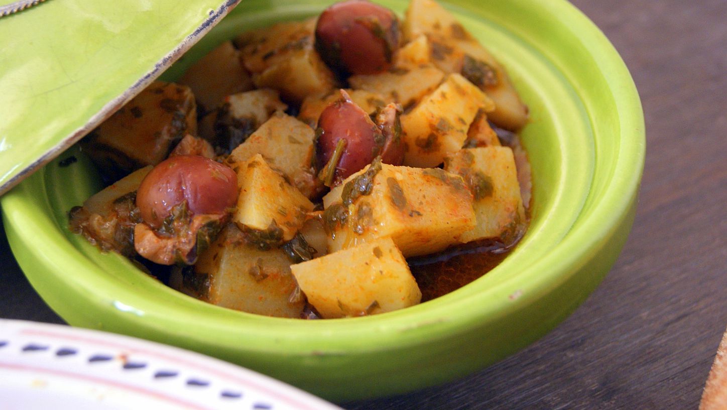 Moroccan potato salad with chermoula. The potatoes are cut in cubes and coated with chermoula, served in a green plate and decorated with purple olives