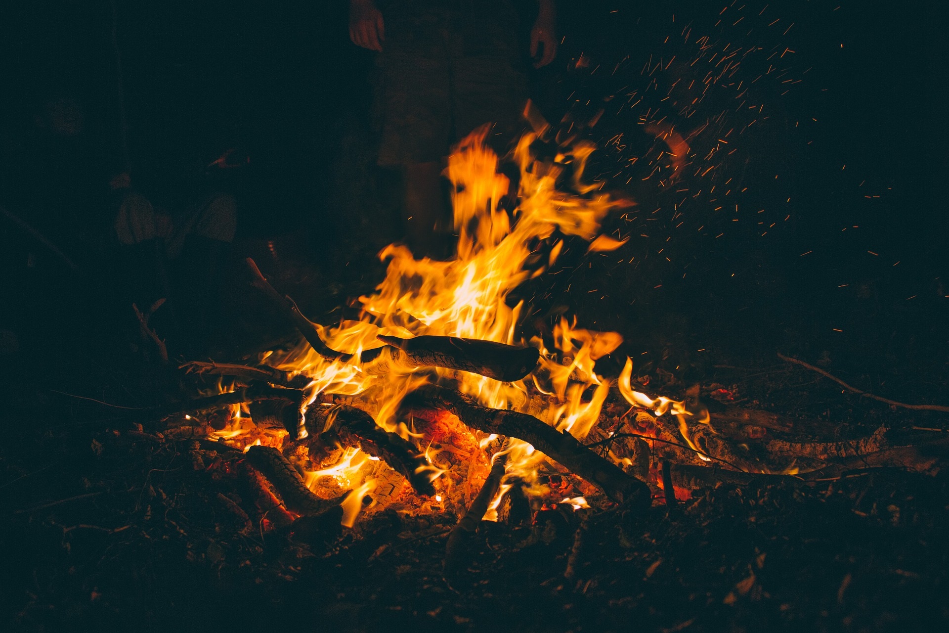 Flames of a bonfire burn bright orange in the dark. Wood can be seen through the flames.