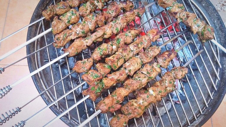 Overhead photo of skewers of marinated beef on a grill. The meat is almost ready to be served.