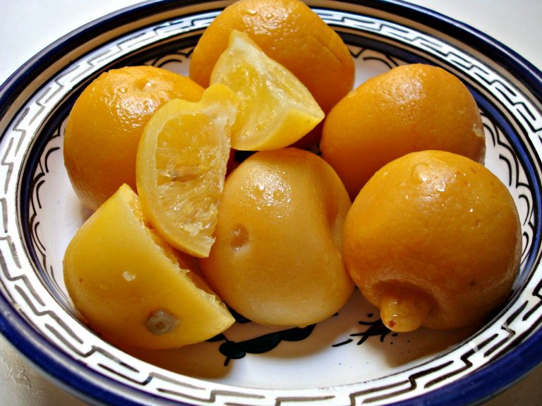 Whole preserved lemons and wedges of preserved lemon in a decorated ceramic dish.