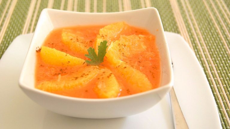 A white bowl holding Moroccan carrot and orange salad. Wedges of orange are arranged in a pinwheel as a garnish.