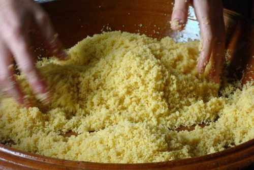 Close-up image of hands tossing grains of couscous in a large shallow bowl.