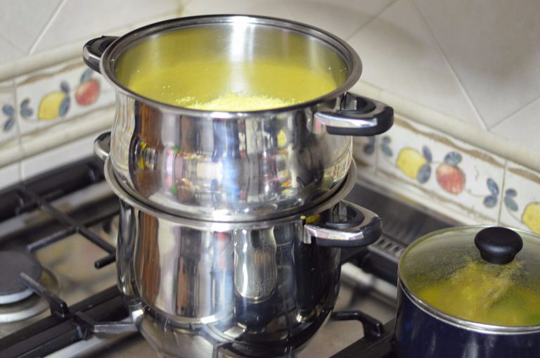A couscoussier is on a stove. Couscous is barely visible in the steamer basket.