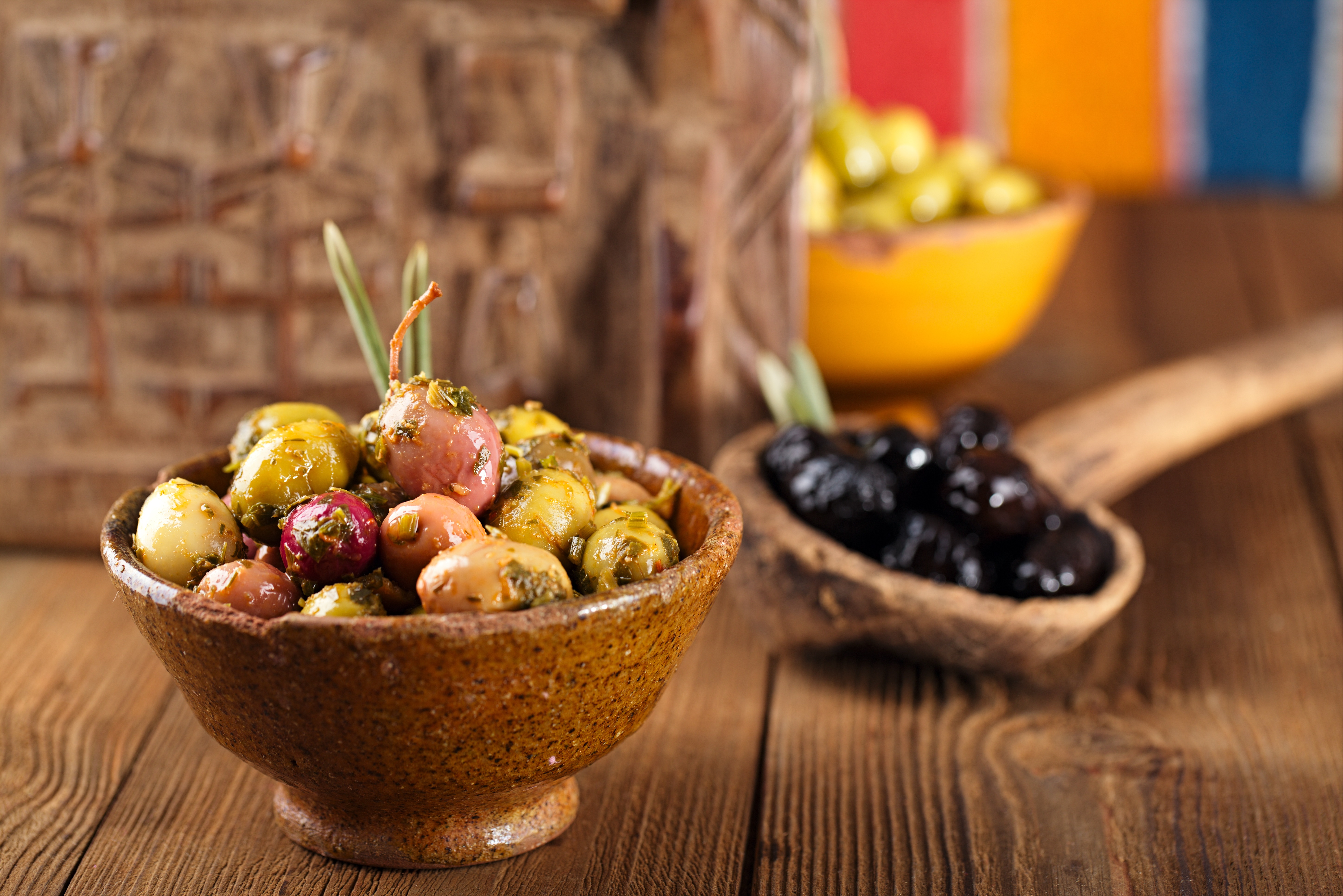 Marinated olives in bowls on wooden surface. The foremost bowl is in focus while two other bowls are shown in the background.