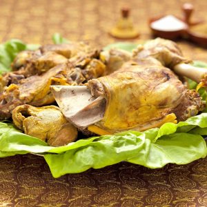 A lettuce-line platter holds large pieces of steamed lamb. Small tagine-shaped condiment dishes holding salt and cumin are in the background.
