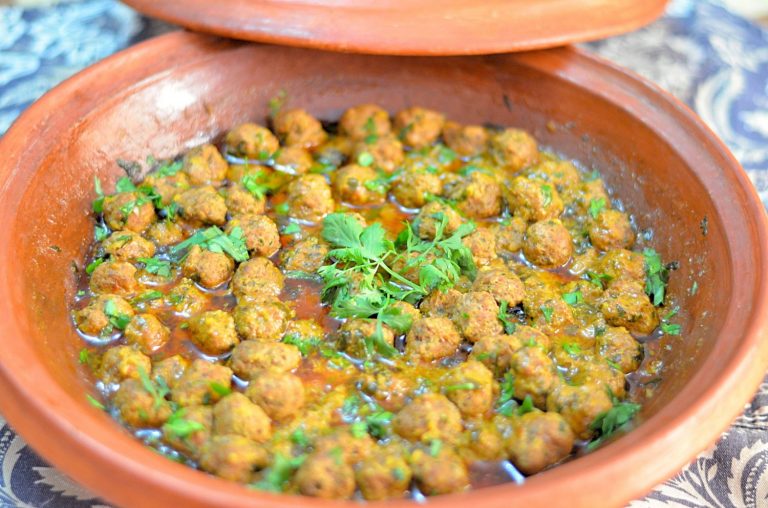 Marble-sized meatballs and buttey sauce in an unglazed tagine. The dish is garnished with a sprig of fresh cilantro.
