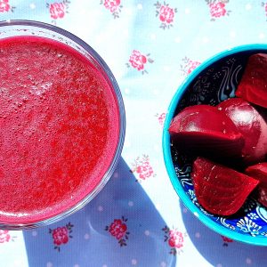 Overhead view of a large glass of Moroccan beetroot juice sitting next to a bowl of cooked beets.