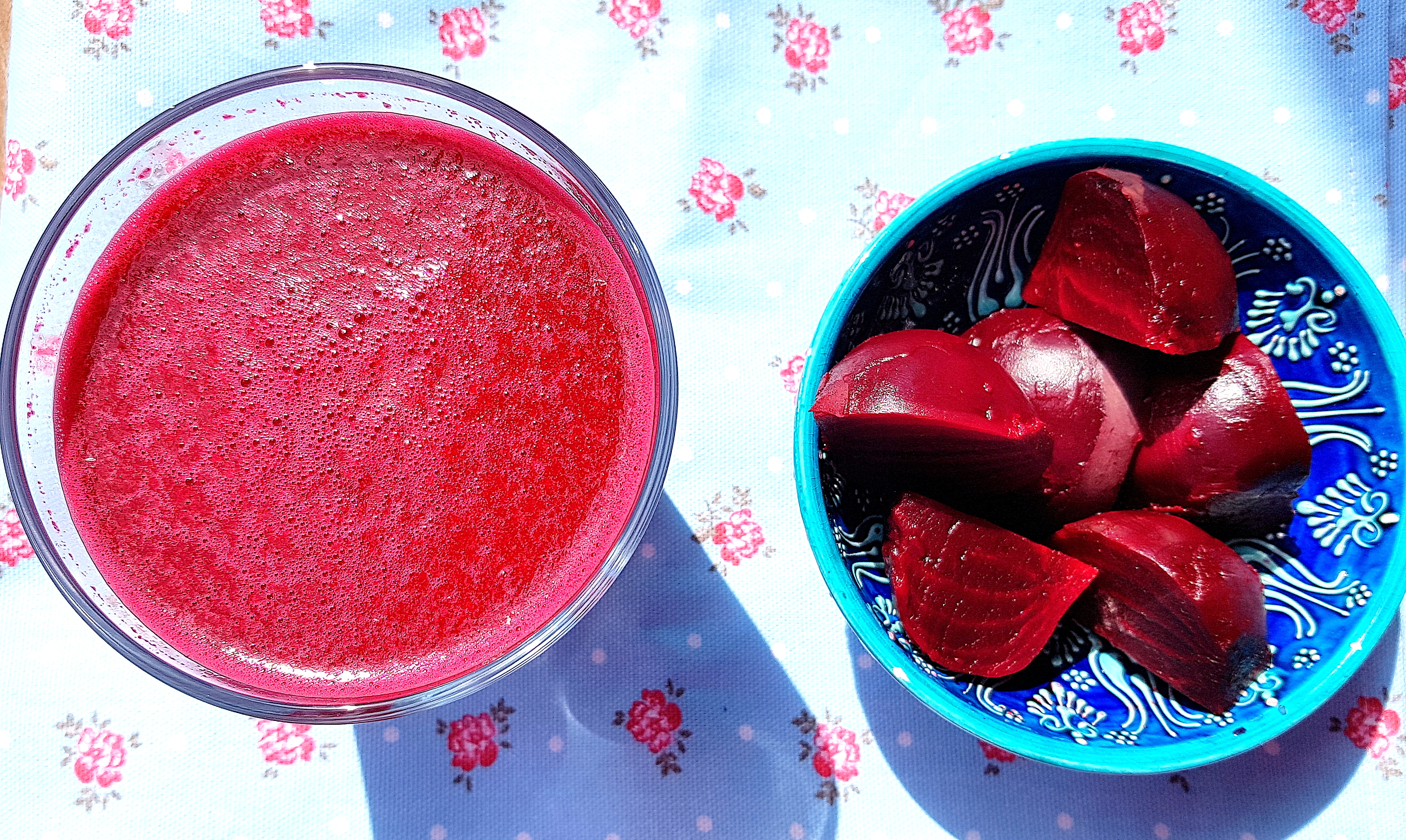 Overhead view of a large glass of Moroccan beetroot juice sitting next to a bowl of cooked beets.
