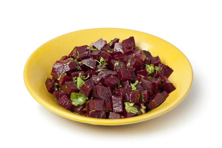A small yellow bowl of Moroccan beet salad. The salad is made of diced, cooked beets which have been tossed with a vinaigrette and garnished with parsley.