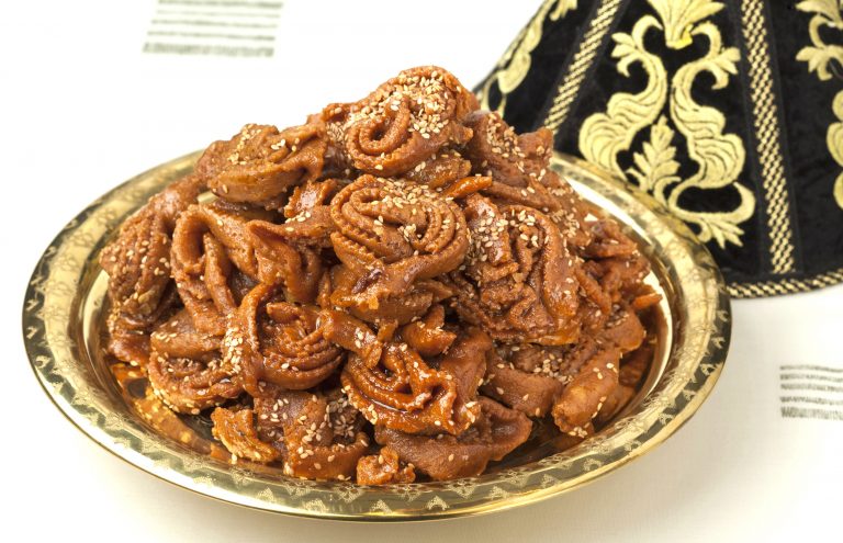 A mound of Moroccan chebakia cookies are mounded on a decorative metal tray.