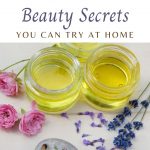 Several jars of essential oils sitting next to lavender and roses.