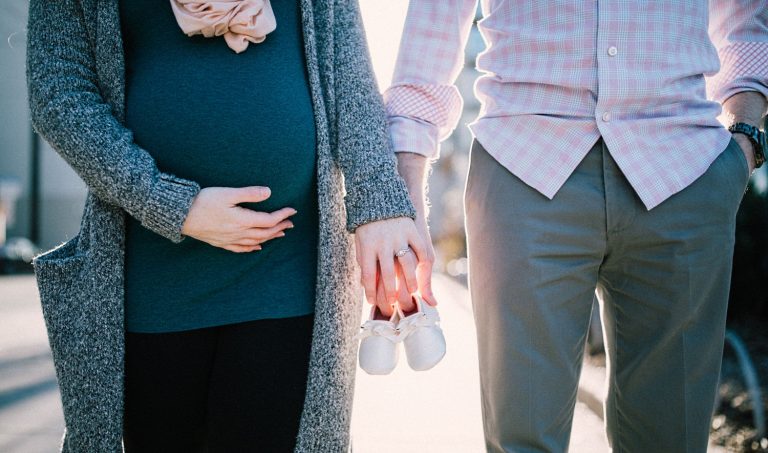 Midriff view of pregnant woman and man holding hands.